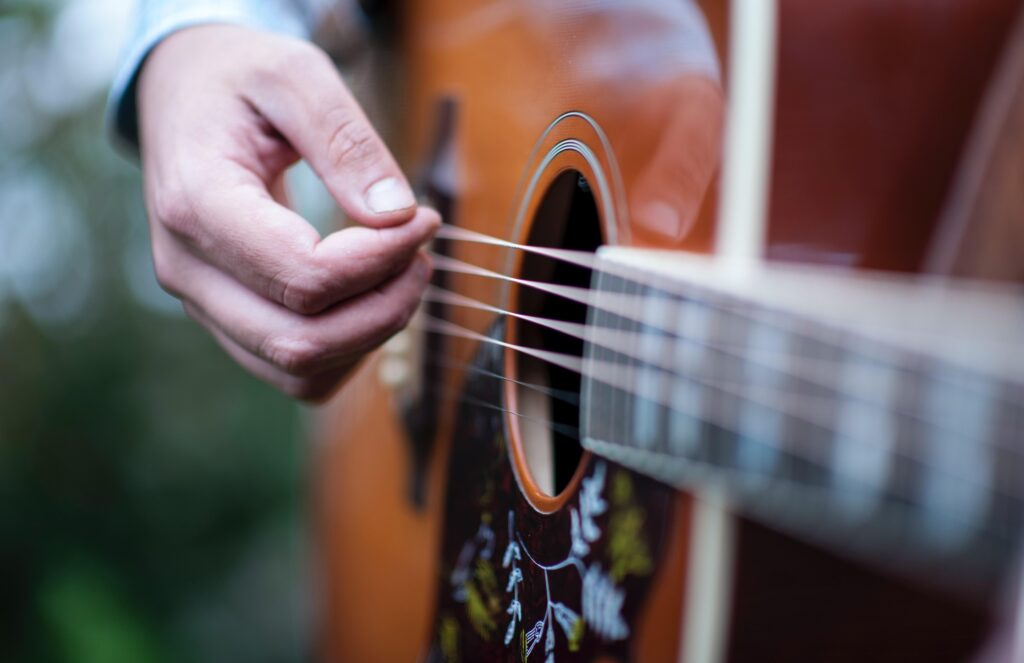 Zbliżenie na gitarę akustyczną oraz dłoń, grającą na niej