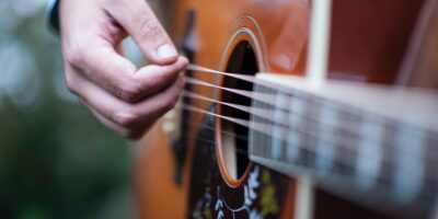Zbliżenie na gitarę akustyczną oraz dłoń, grającą na niej