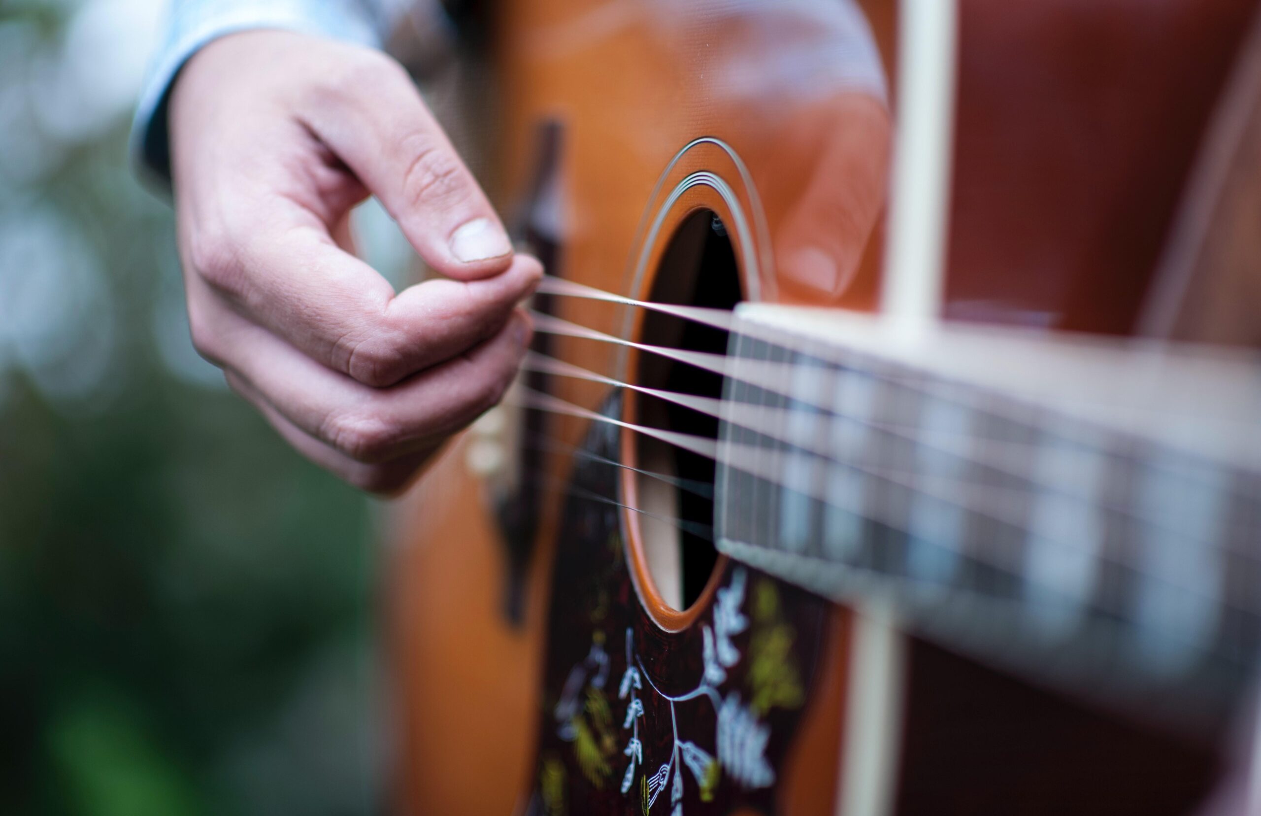 Zbliżenie na gitarę akustyczną oraz dłoń, grającą na niej